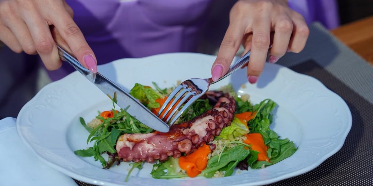 Woman enjoying an octopus salad with fresh greens outdoors. Vibrant and appetizing.