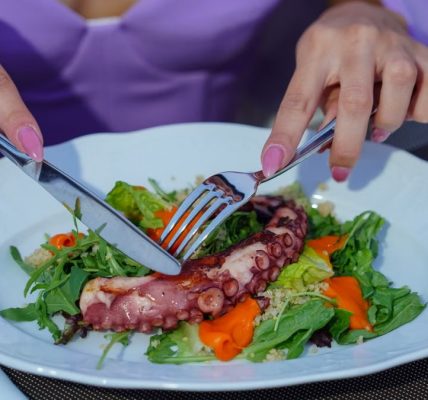 Woman enjoying an octopus salad with fresh greens outdoors. Vibrant and appetizing.