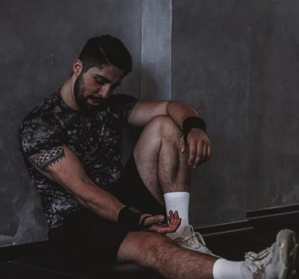A muscular man in a gym environment taking a moment of rest, reflecting in a dark moody setting.